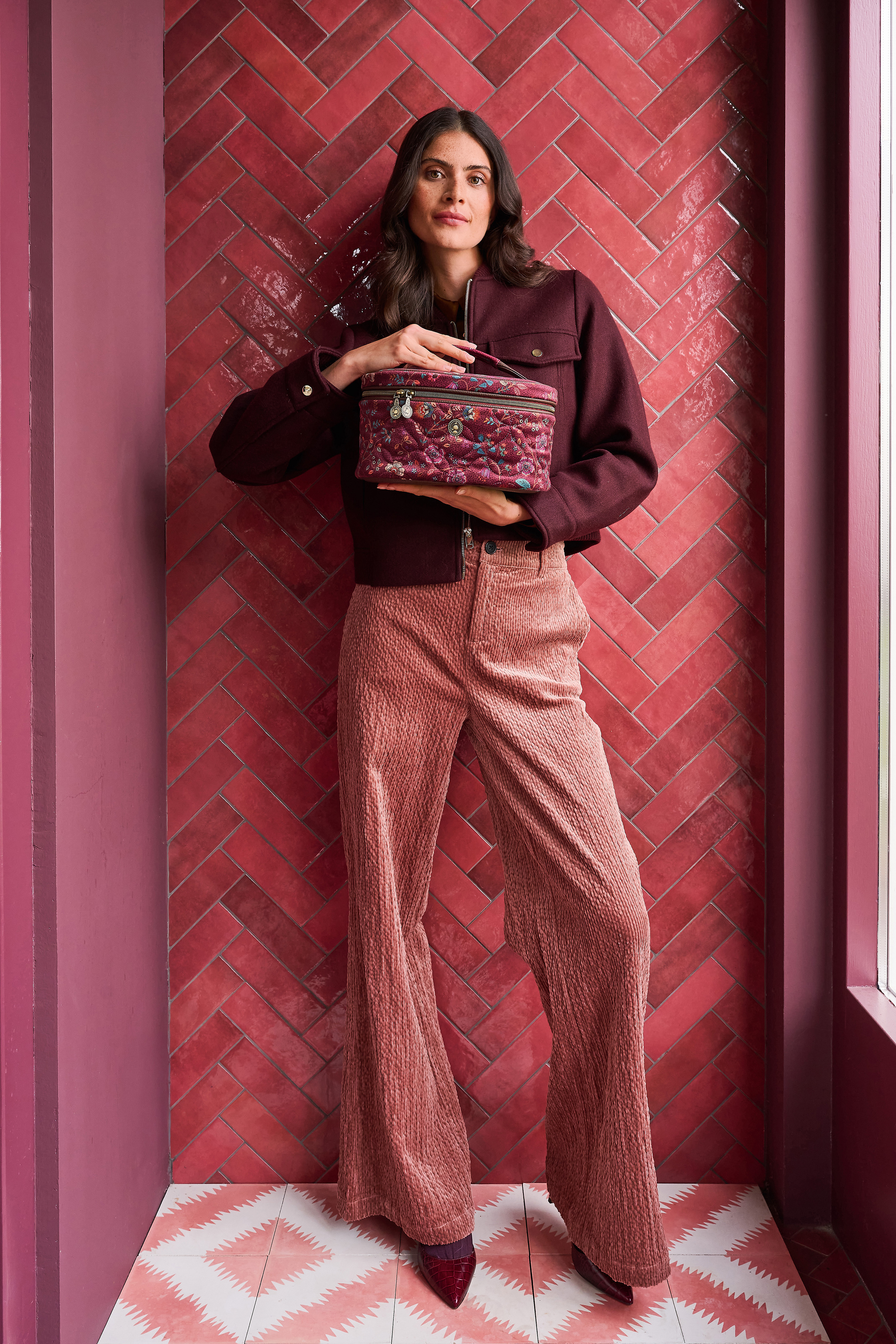 Pip Studio Cleo Flora Bangelore kosmetický kufr, tmavě růžový drží ho modelka v rukou a má na sobě vínovou bundu a růžové kalhoty