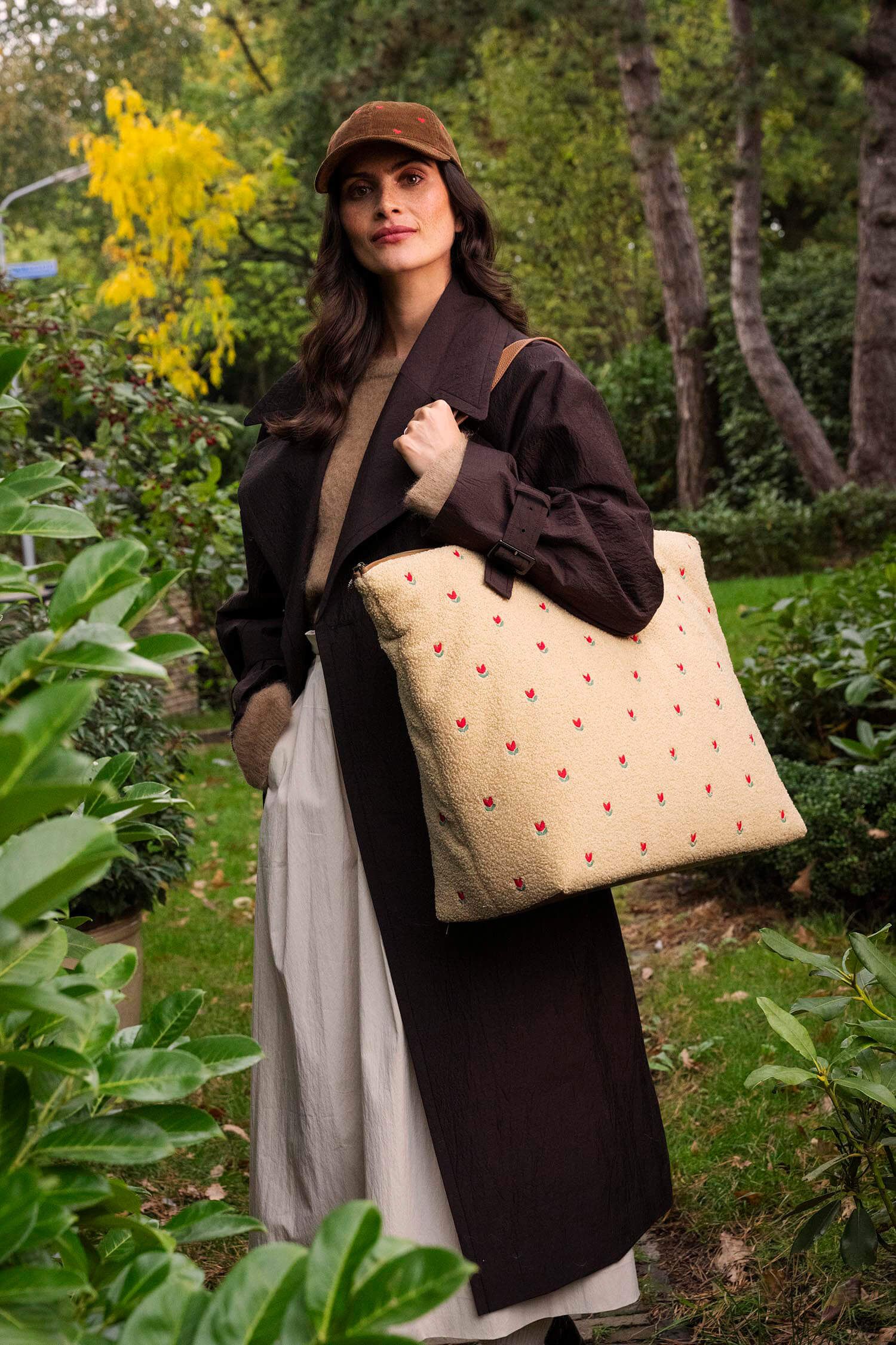 Pip Studio Tilda Tote Bag Teddy Sand velká cestovní taška, písková na modelce v tmavě hnědém kabátu a kšiltovce se srdíčkami v přírodě
