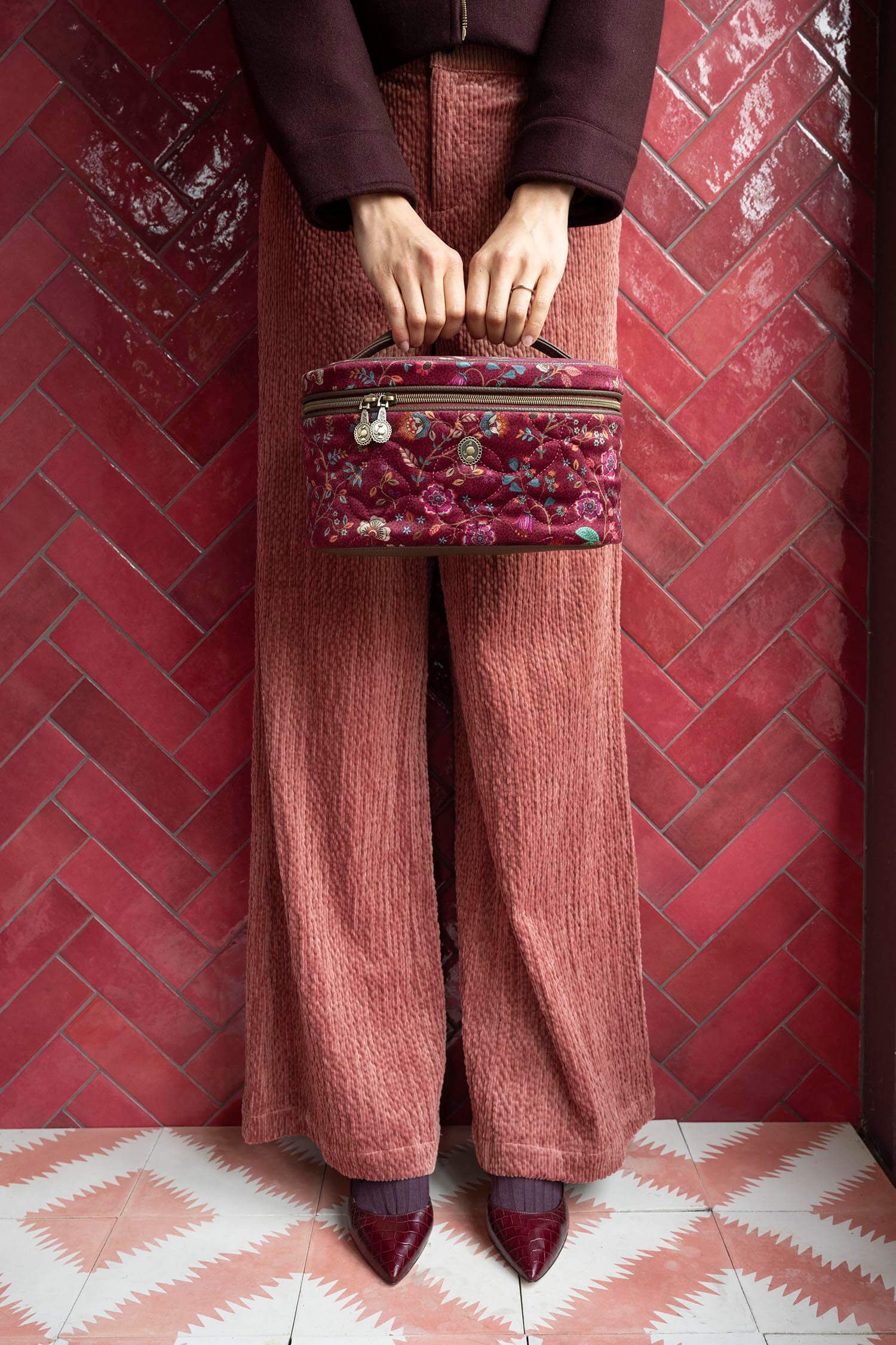Pip Studio Cleo Flora Bangelore kosmetický kufr, tmavě růžový drží ho modelka v rukou a má na sobě vínovou bundu a růžové kalhoty pohled zespoda