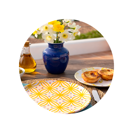 Banner Jarní kolekce – talíře se žlutým geometrickým dekorem na venkovním stole s květinami ve váze a dezerty, upozornění na limitovanou edici.