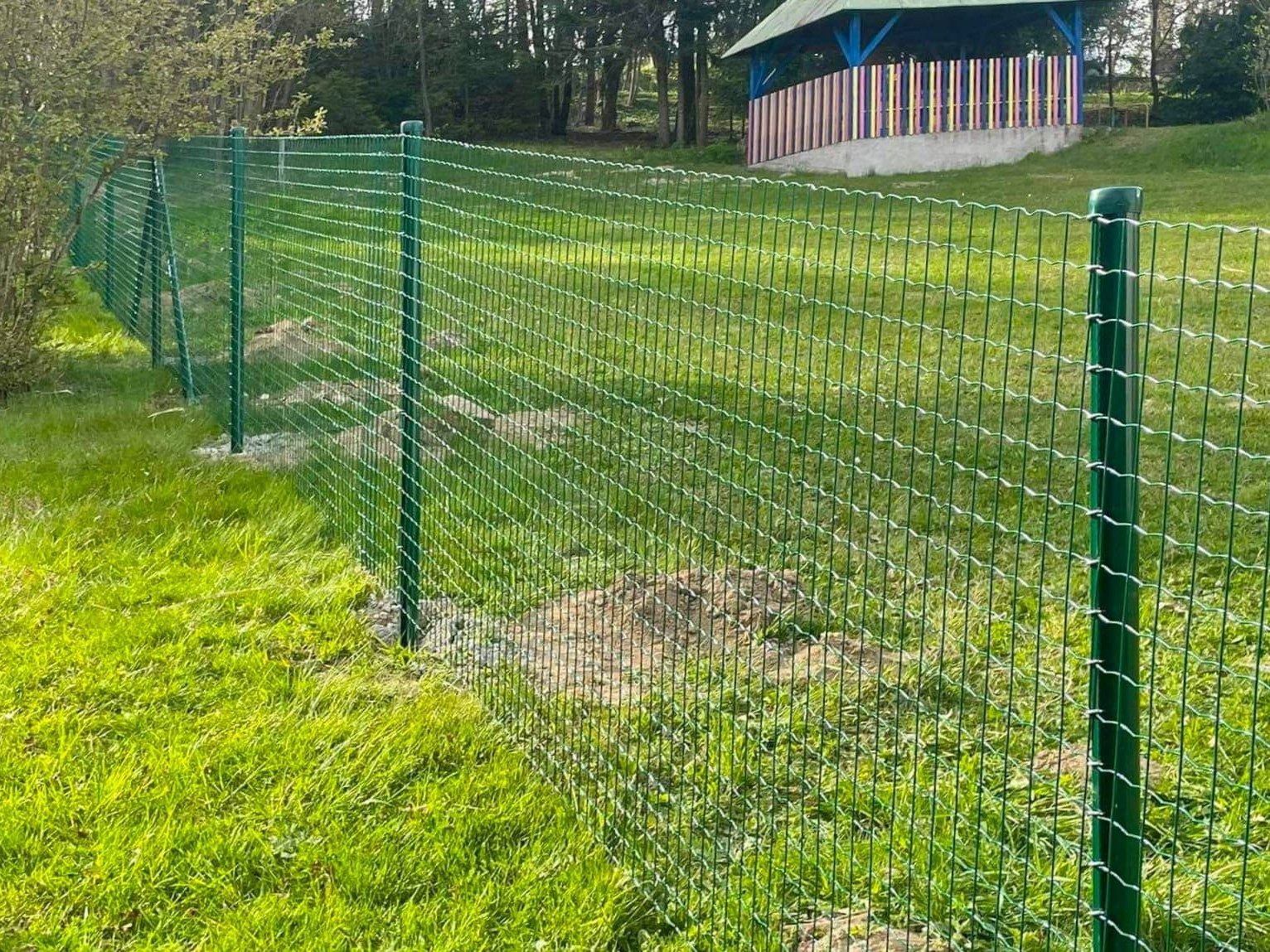 Zelené zvárané pletivo na stĺpikoch okolo trávnatého pozemku