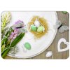 Velikonoční prostírání z PVC s motivem jemného jarního aranžmá, které zahrnuje hnízdo se zelenými a bílými vajíčky, motýly a svěží květiny na rustikálním dřevěném podkladu.