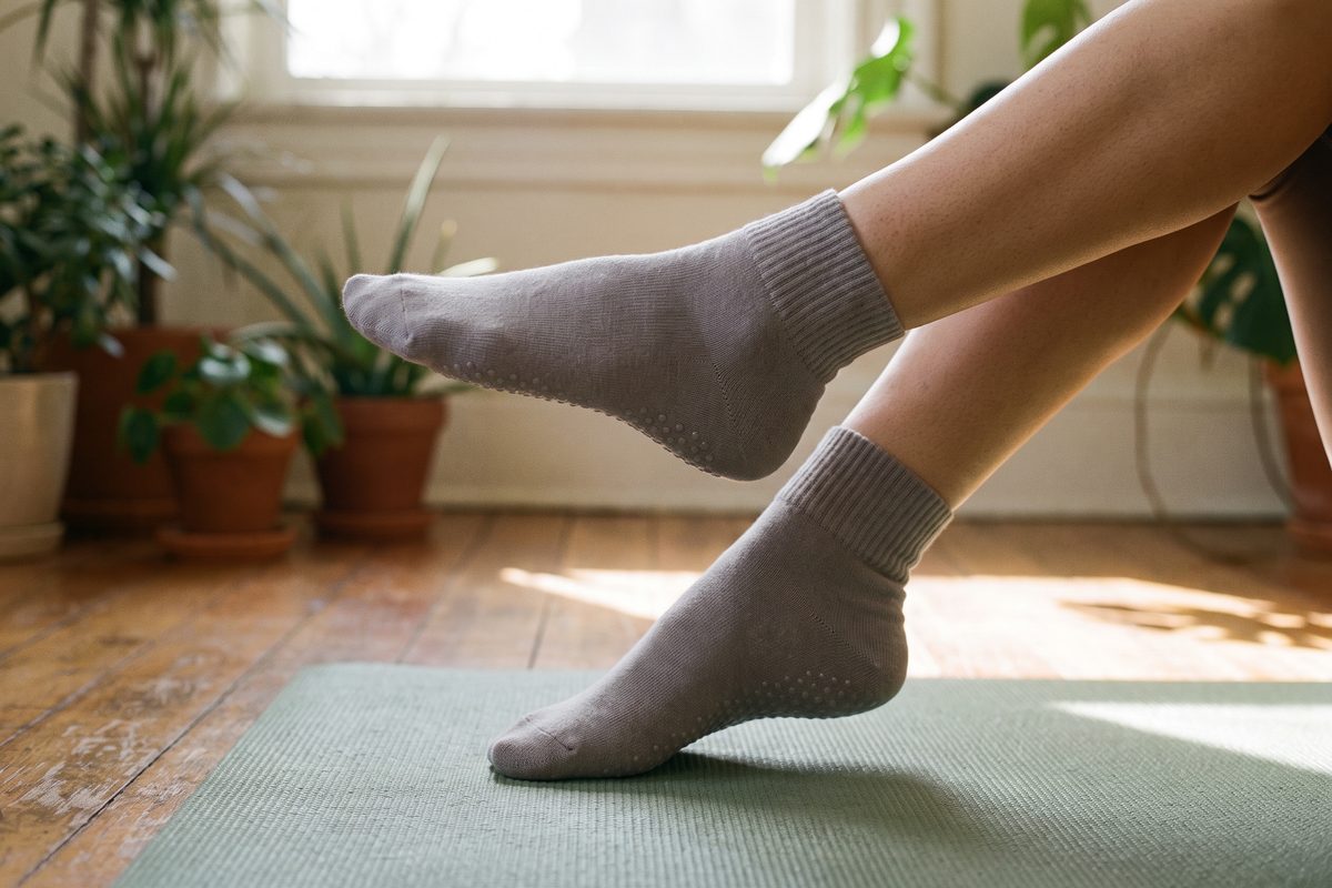 Nohy v šedých ponožkách s protiskluzovými body na podložce na pilates