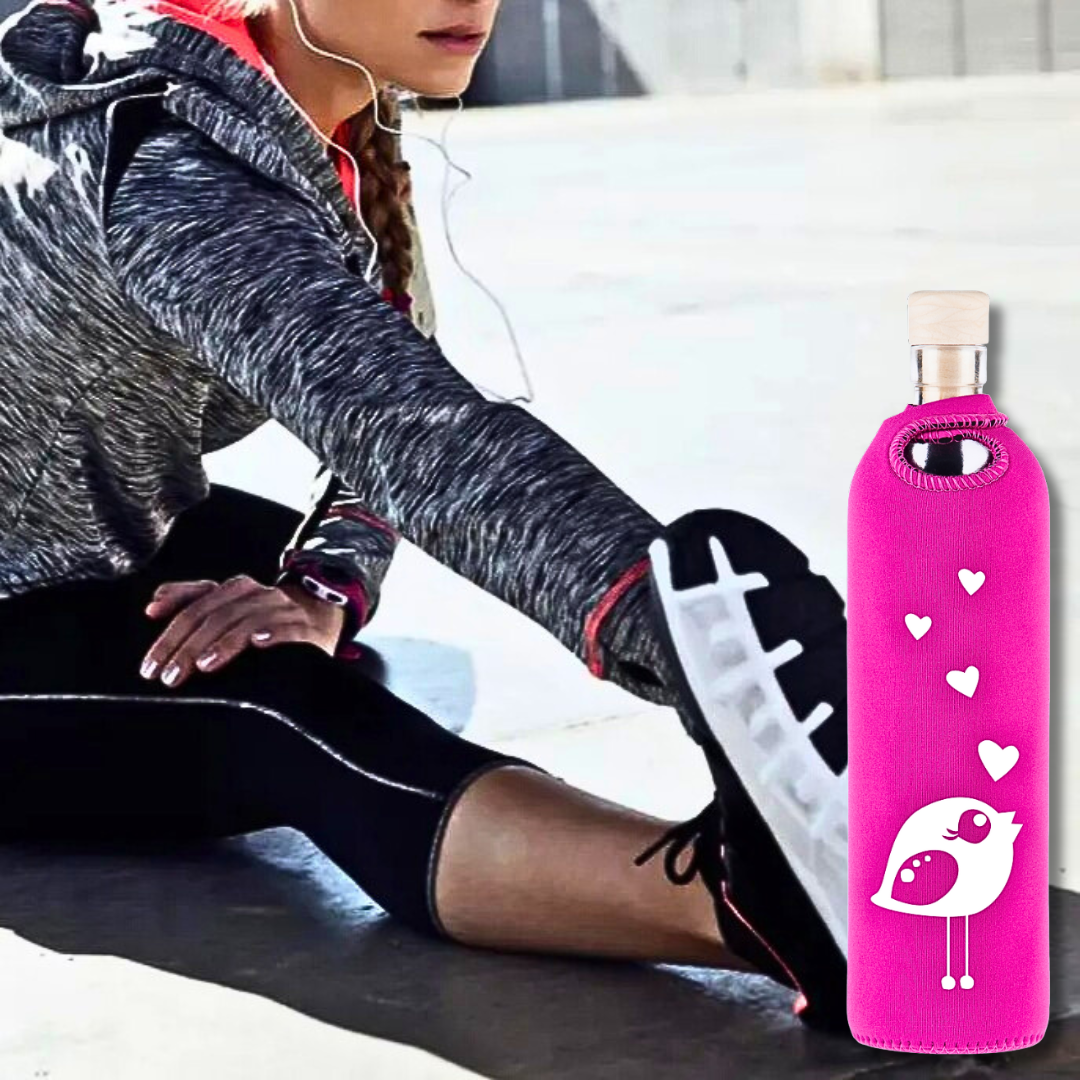 Woman stretching with a pink Flaska glass water bottle (bird design) in a neoprene sleeve.