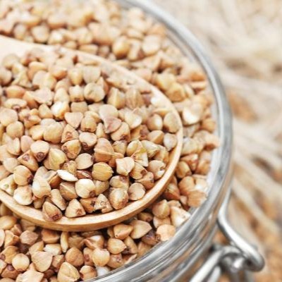Close-up of raw organic buckwheat kernels in a glass jar with a wooden spoon.
