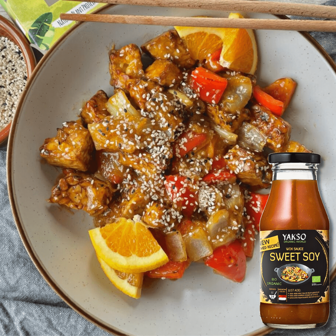 Crispy tempeh stir-fry with peppers, orange slices and sesame seeds on a plate, with a Yakso Sweet Soy Wok Sauce bottle