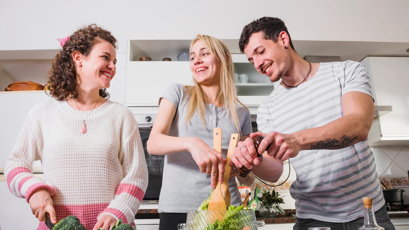 two-female-friends-her-man-preparing-salad-kitchen_23-2147947801