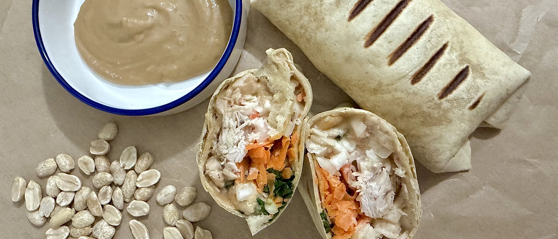 Rozkrojený wrap s kuřecím masem, mrkví a arašídovým dipem
