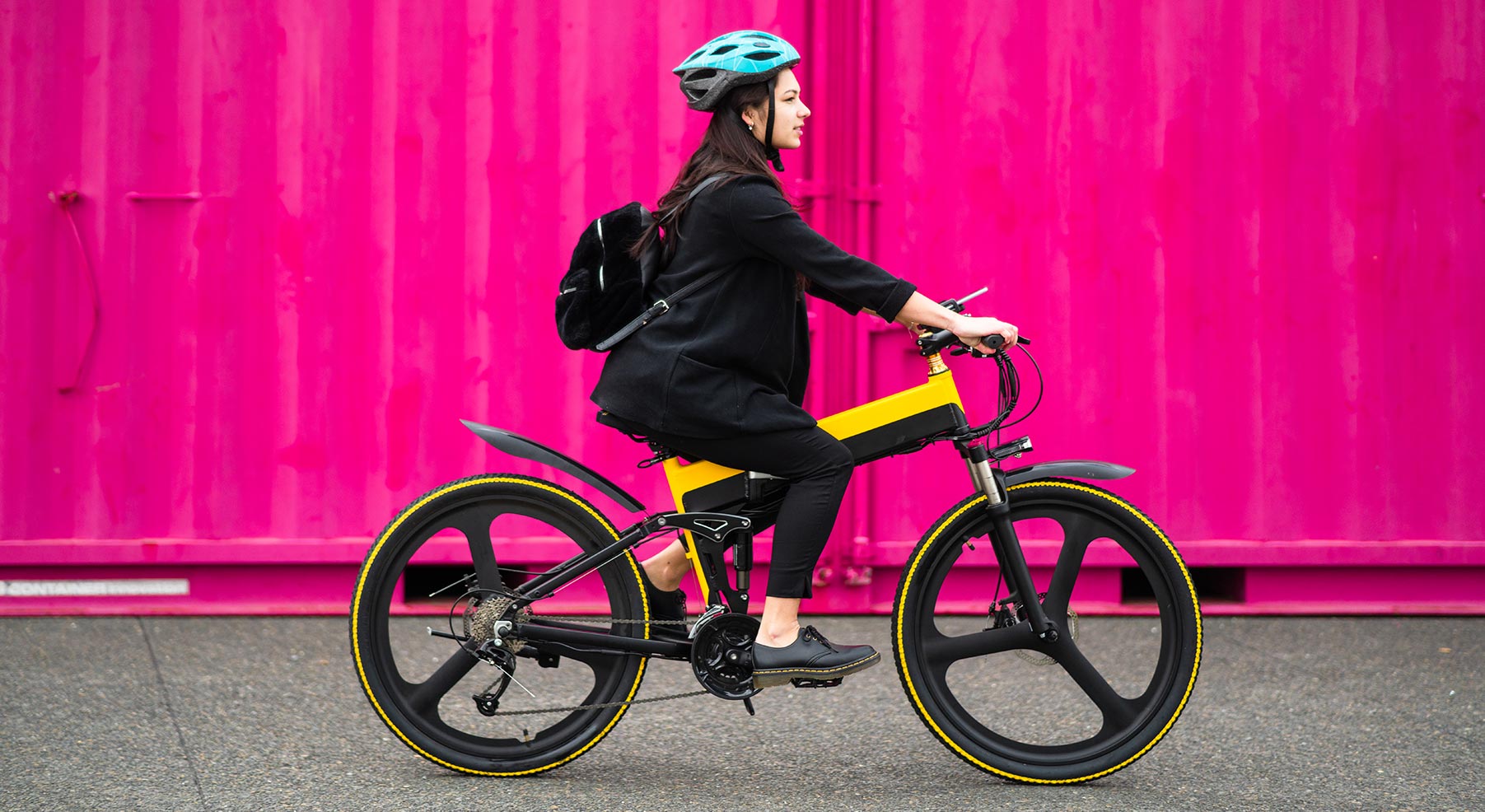 woman-riding-ebike-pink-background-iStock-1312730362