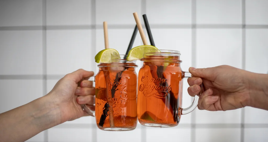 Domácí limonáda ve dvou zavařovacích sklenicích s uchem, brčky a plátky limetky