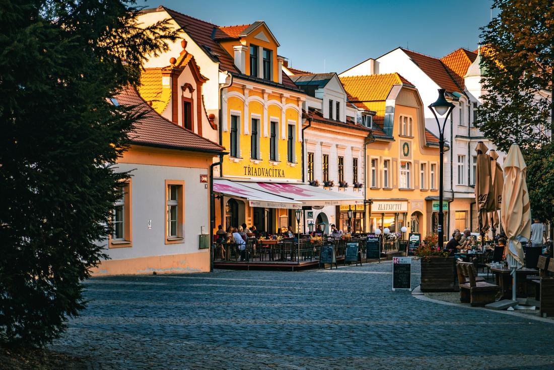 Historické náměstí českého města s předzahrádkami restaurací v podvečerním světle