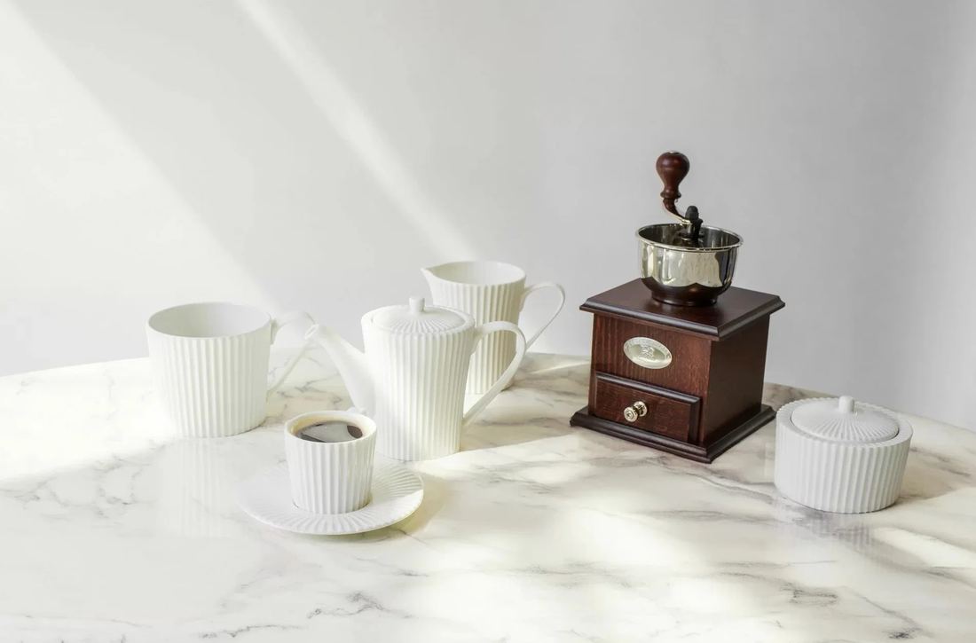 Bílá kávová souprava z kostního porcelánu RAK na mramorovém stole s mlýnkem na kávu