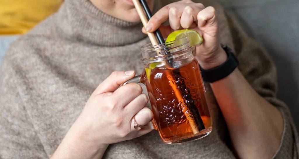 Žena drží zavařovací sklenici s uchem plnou domácí limonády s citronem a brčky