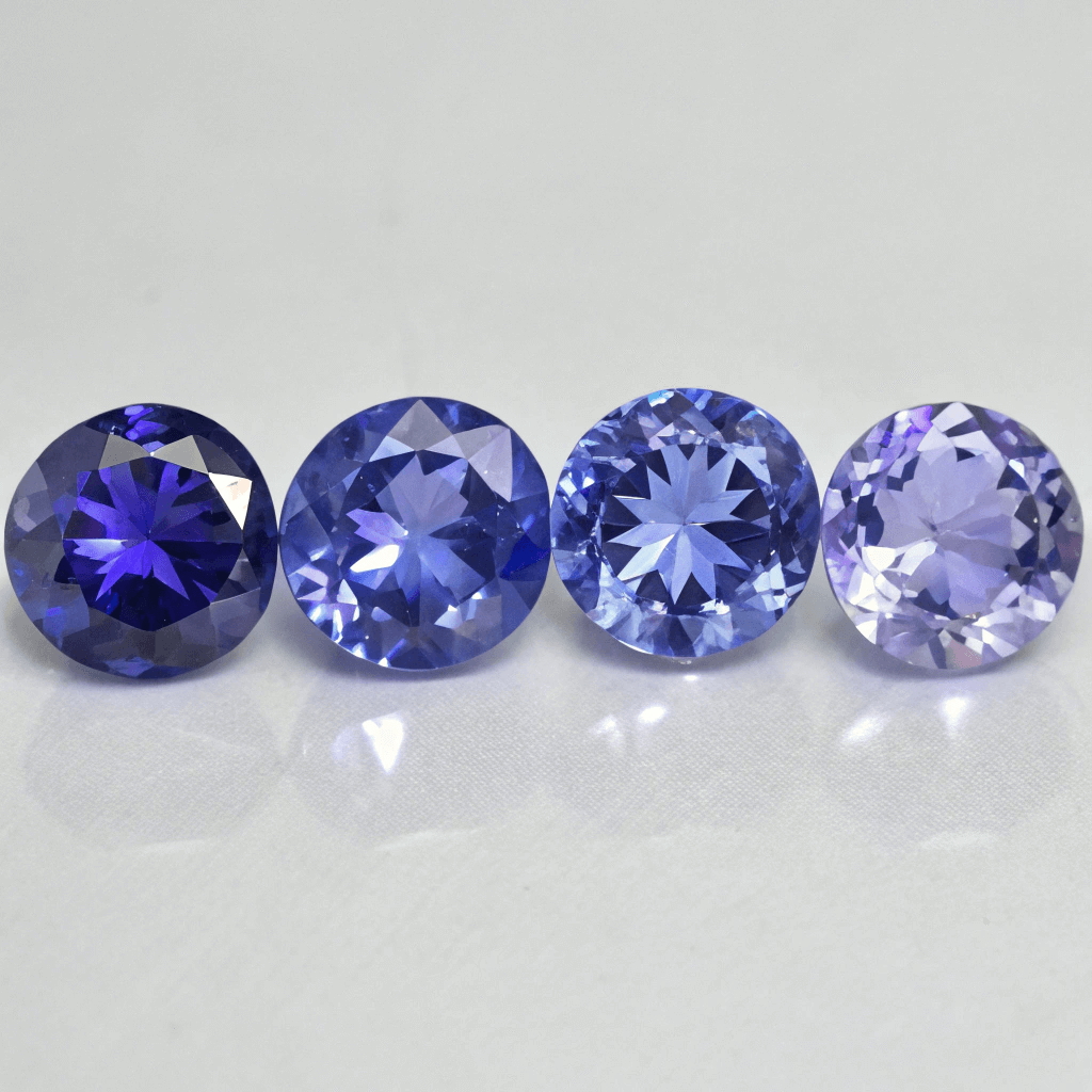 Čtyři broušené tanzanity vedle sebe ukazující rozdíly v sytosti barvy od tmavě modrofialové po světle fialovou.
