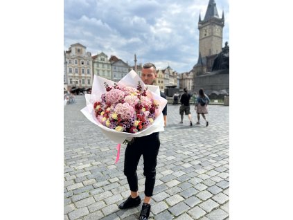 Muž držící elegantní míchanou kytici s růžemi a chryzantémami na Staroměstském náměstí.
