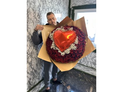 Muž držící „Valentýnský puget 101 růží“, zdobený rudými růžemi a středovým červeným srdcem, zachycený uvnitř luxusního interiéru.