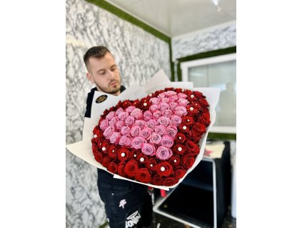 Muž drží velký puget ve tvaru srdce z rudých a růžových růží v interiéru květinářství.