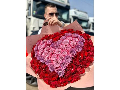 Muž držící třpytivý puget růží ve tvaru srdce, kombinace rudých a světle růžových růží.