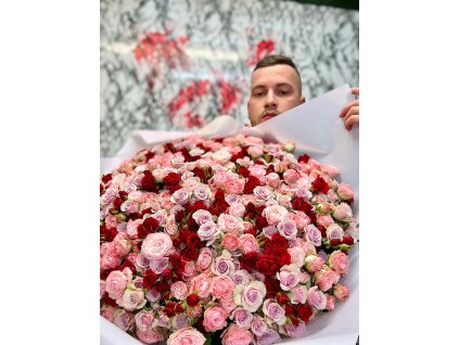 Muž držící kytici trsových růží v jemných růžových a červených odstínech, aranžovaných do elegantního balení.