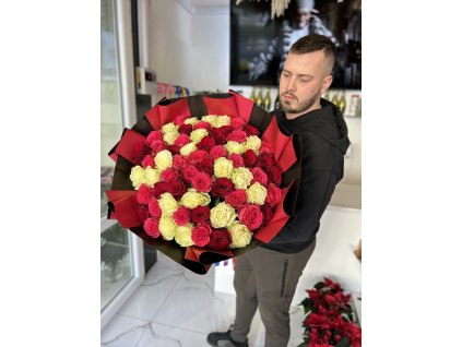 Muž drží tříbarevnou kytici 101 růží v kombinaci rudých, růžových a bílých květů v elegantním interiéru.