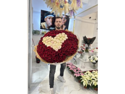 Luxusní kytice ve tvaru srdce z rudých růží se světle růžovým středem, držena v elegantním prostředí květinářství.