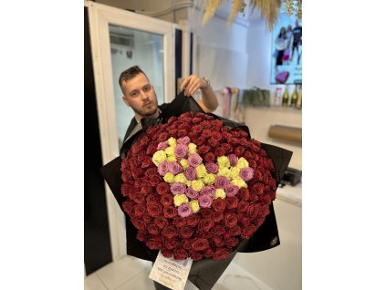 Luxusní kytice ve tvaru srdce z bílých, fialových a rudých růží, držená mužem v elegantním prostředí.
