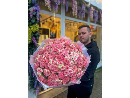 Luxusní puget růžových trsových růží v růžovém balení, držený před květinářstvím Růže Michael.