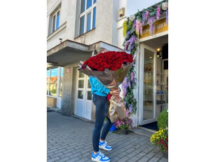 Pugét 101 rudých růží s extra dlouhými stonky v luxusním metalickém balení před butikem Růže Michael