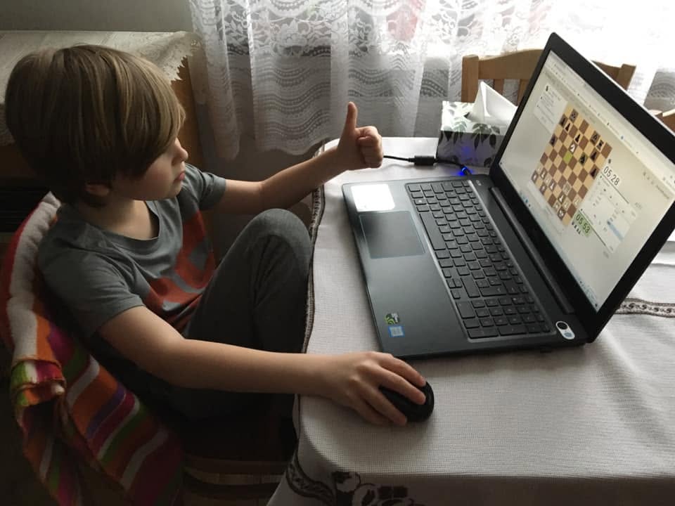 Băiat care joacă o partidă de șah online pe laptop și arată că îi place