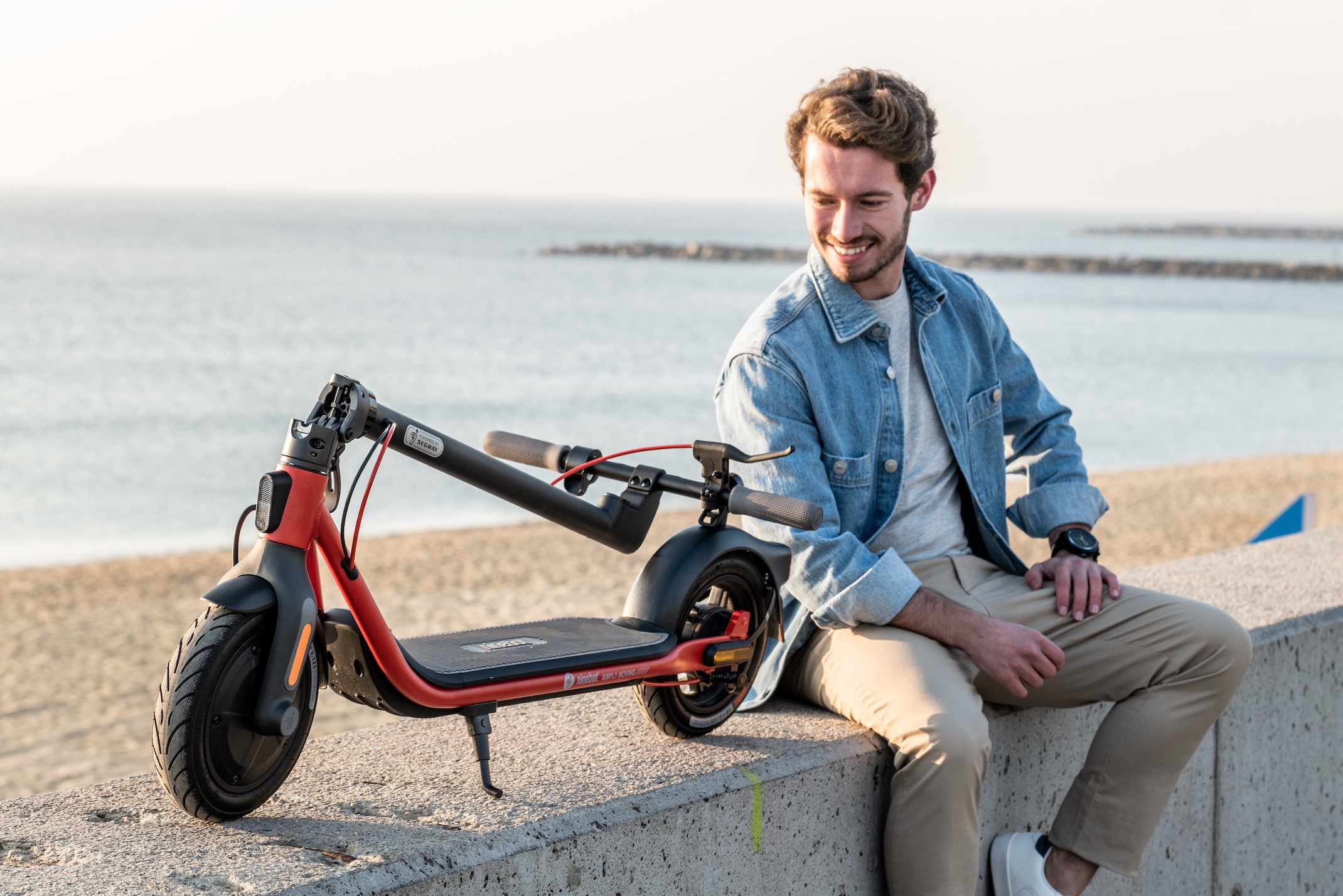 Ninebot KickScooter D series Powered by Segway_Lifestyle picture_ Man sitting besides folded kickscooter