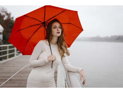 portrait of young woman with red umbrella leaning on railing during rainy day TCEF00034