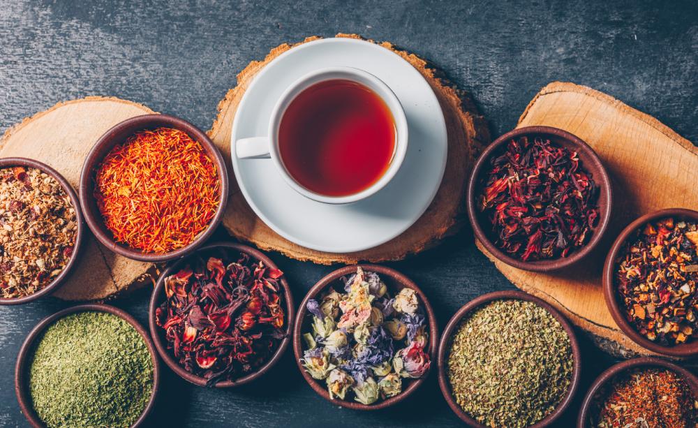šálka čaju a misky s rôznymi sypanými čajmi na textúrovanom povrchu
