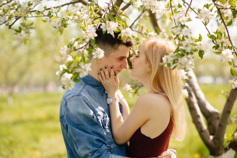 mladá žena s blond vlasmi stojí pod rozkvitnutou čerešňou s priateľom