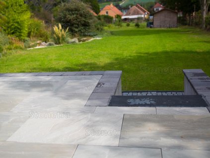 Paving slabs in Sandstone Greyl Roman pattern form a garden edge terrace next to the lawn