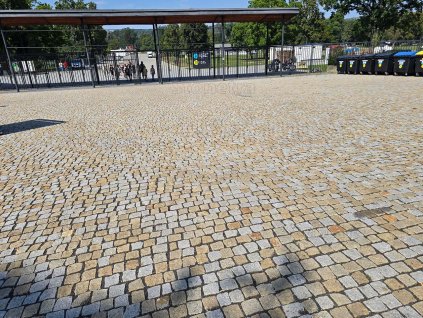 Large plaza paved with mixed yellow-grey granite cobblestones 4–6 cm — durable natural-stone setts with tight joints.