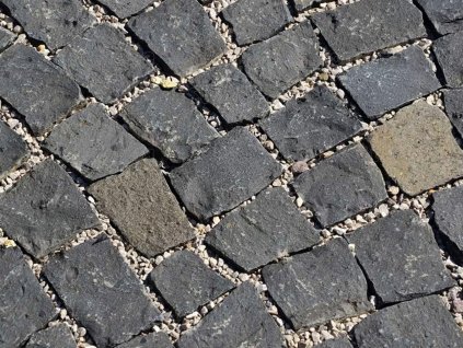Close-up of small-format black basalt cobblestones laid with gravel joints - durable natural-stone paving.