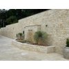 Stacked stone exterior wall made of Sandstone Crema with smooth concrete driveway and greenery.