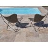 Pool deck pavers — Travertine Noche French pattern with two chairs by the water, sunny scene.