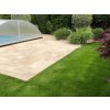 Garden patio slabs in Travertine Noche French pattern installed beside a pool and lawn.