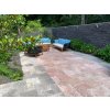 Patio stone pavers in Travertine Red French pattern, tumbled, used on a garden terrace with greenery and seating.