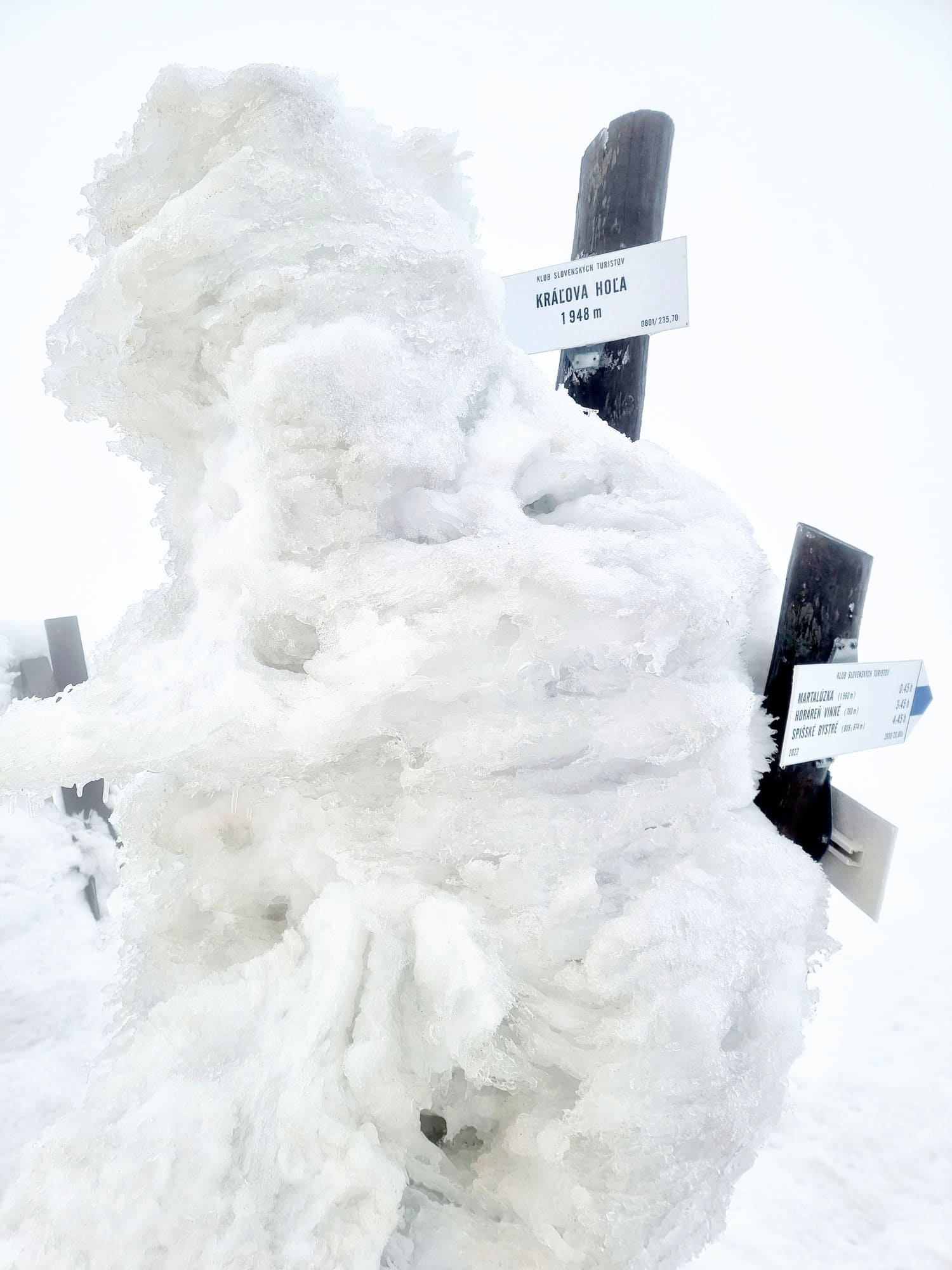 Turistický smerovník na vrchole Kráľovej hole pokrytý snehom a námrazou.