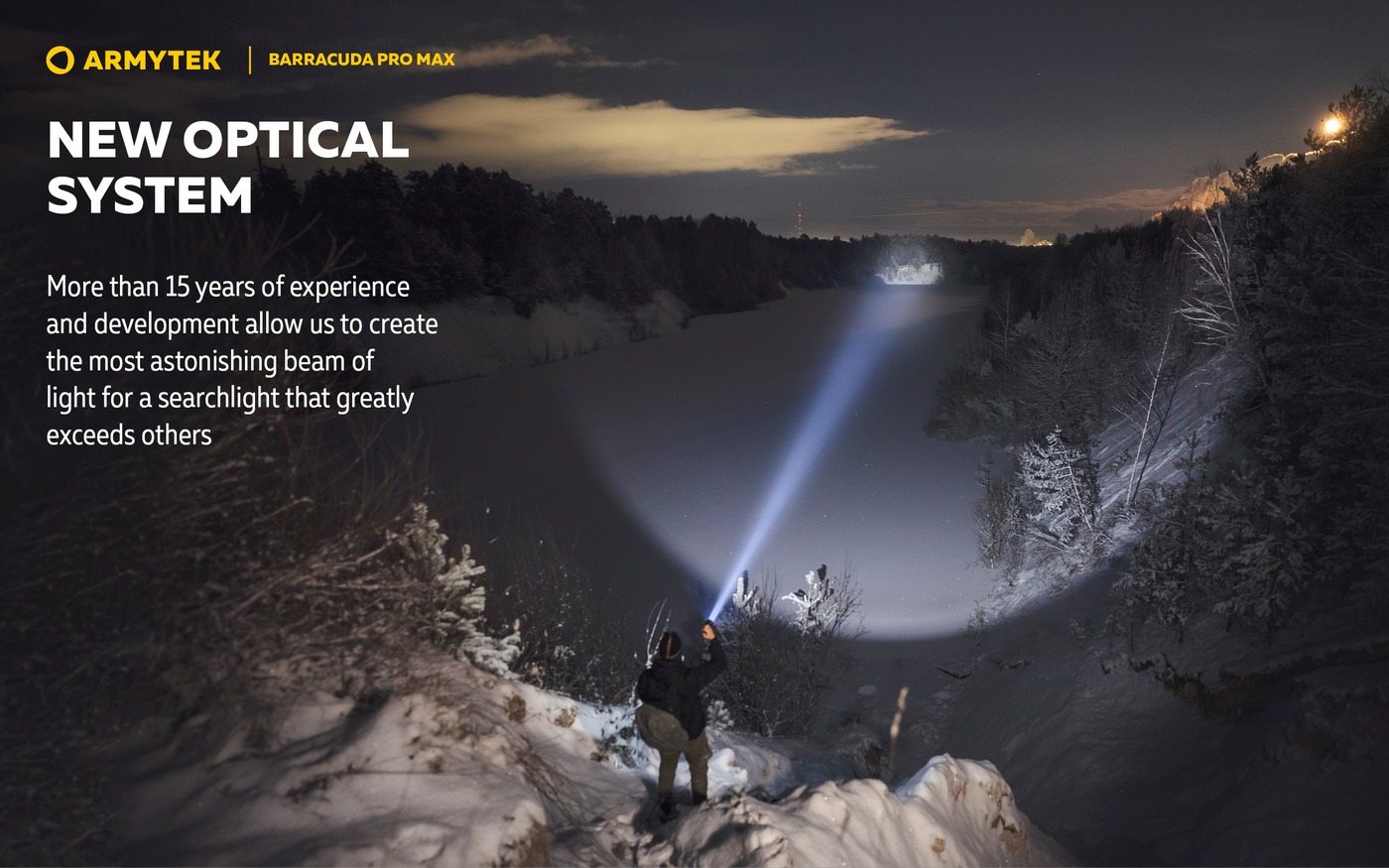 Muž na zasneženom svahu svieti baterkou Armytek Barracuda Pro Max cez zamrznuté jazero na vzdialený breh