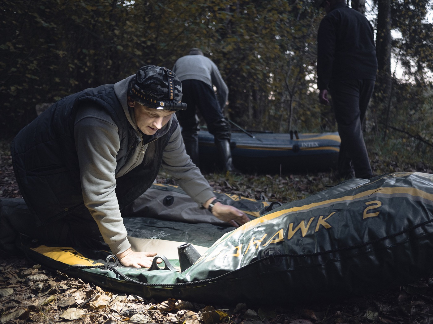 Čelovka Armytek Wizard C2 Pro Max na čelenke cez maskáčovú čiapku pri rozkladaní nafukovacieho člna v lese