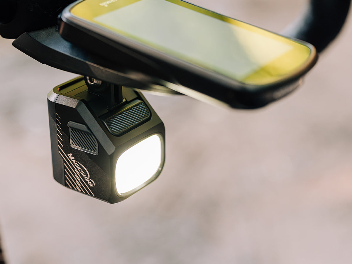 Rozsvietené Magicshine EVO 1100 visí pod predsadeným držiakom, navrchu je cyklopočítač so zapnutým displejom