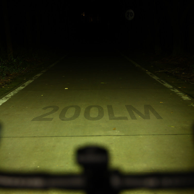 Nočn&aacute; cesta osvetlen&aacute; najniž&scaron;&iacute;m stupňom Magicshine HORI 900, do asfaltu je vp&iacute;san&yacute; n&aacute;pis 200LM