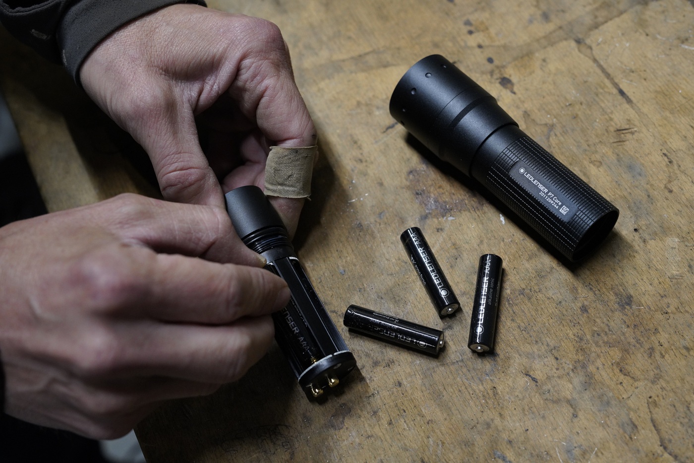 Ledlenser P7 Core na verstaku, ruky zasúvajú zásobník s batériami AAA do hlavovej časti baterky