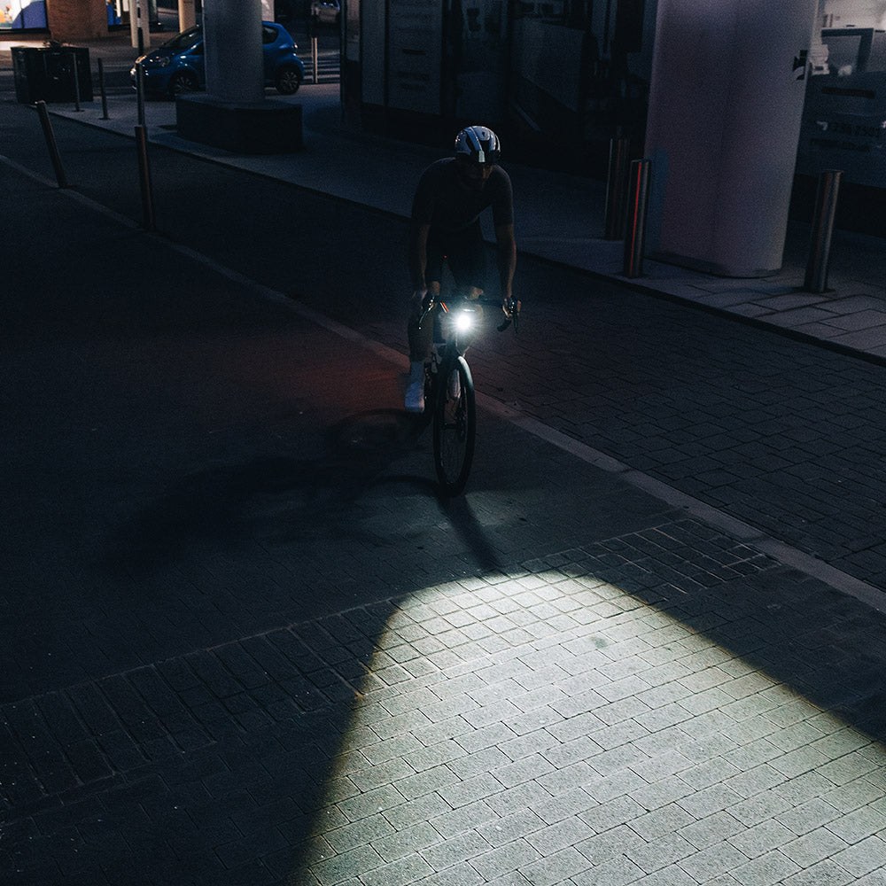 Magicshine EVO 1700 UT v nočnej mestskej ulici — pred kolesom cyklistu leží široký svetelný koberec s ostrou hranou