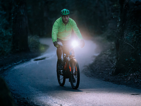 Cyklista na elektrobicykli osvetľuje lesnú cestu za šera svetlom Magicshine ME 2000 s dosvitom 220 m