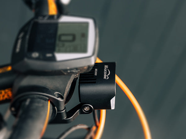 Svetlo Magicshine ME 2000 na riadidlách elektrobicykla vedľa displeja cyklopočítača za dňa