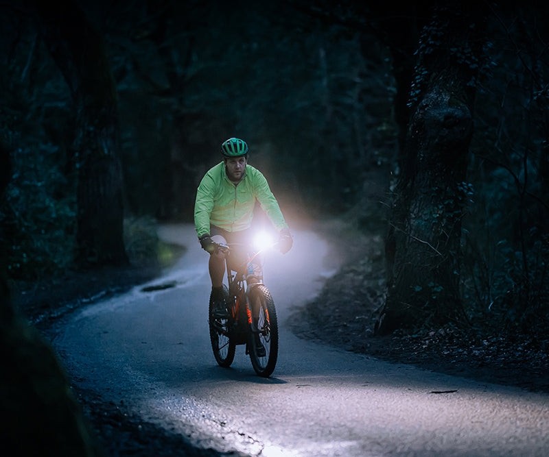 Cyklista na elektrobicykli osvetľuje nočnú lesnú cestu svetlom Magicshine ME 2000 V2.0